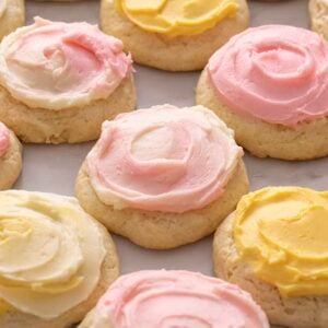 A group of sour cream cookies topped with pink and yellow buttercream on a marble surface.