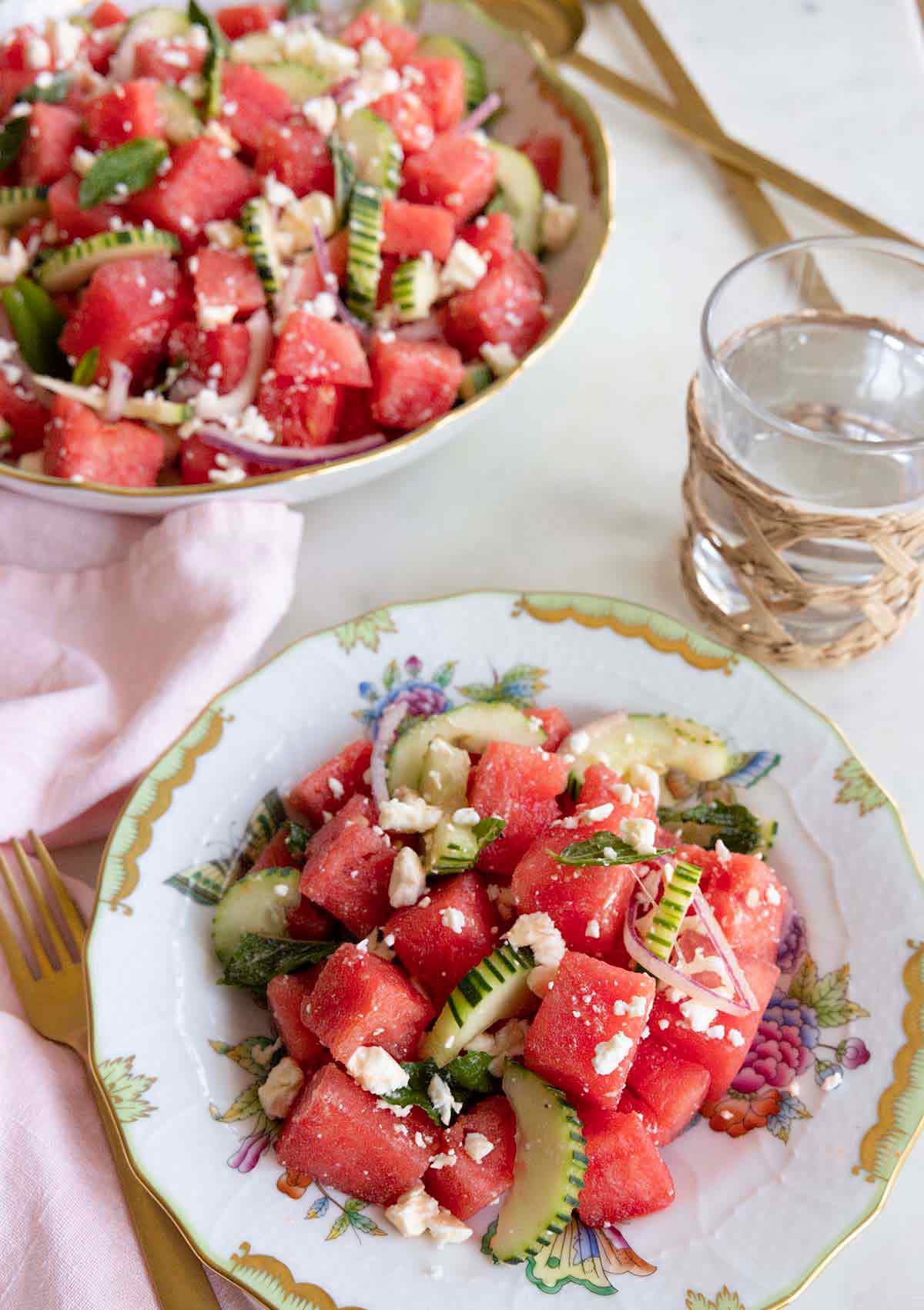 A plate of watermelon salad beside a glass of water and a bowl of watermelon salad.