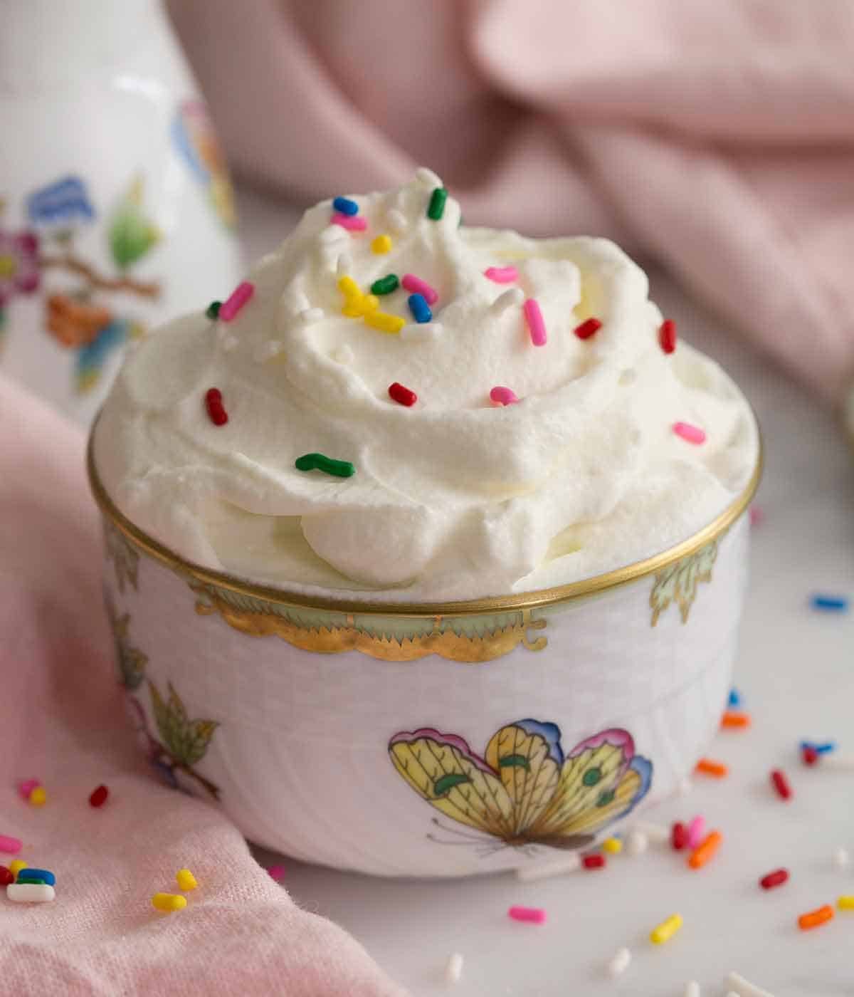 A bowl with flowers and butterflies containing whipped cream and rainbow sprinkles.