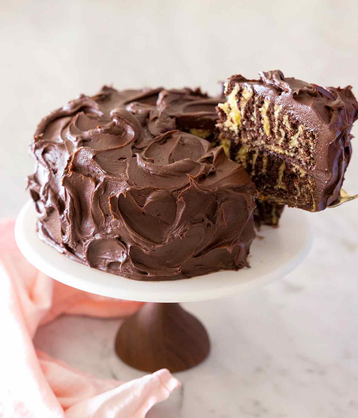 A zebra cake on a cake stand with one slice being lifted up.