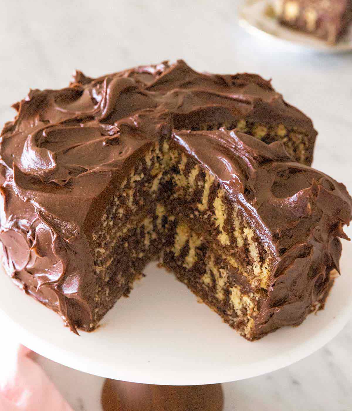 A zebra cake on a cake stand, cut up, with a slice on the stand.