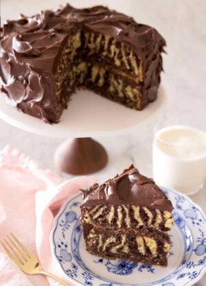 A slice of zebra cake on a plate in front of the rest of the cake behind it on a cake stand.
