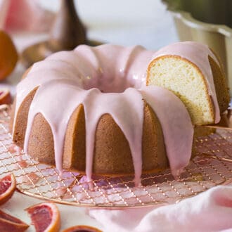 A blood orange pound cake topped with soft pink glaze getting a piece removed.