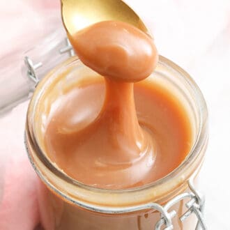 A jar of caramel with a golden spoon removing some.
