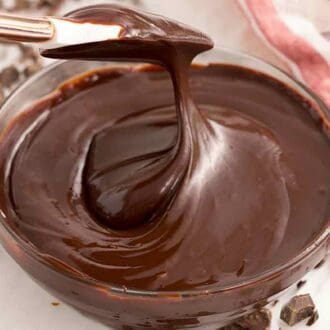 A glass bowl of chocolate ganache with a spatula lifted up.