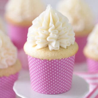 A group of delicious vanilla cupcakes in pink paper sleeves topped with spires of vanilla buttercream.