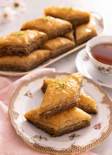 A plate with three baklava with one on top of two, with a platter of baklava in the background.