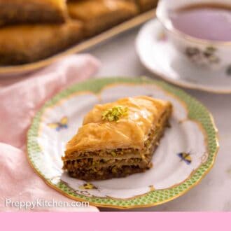 Pinterest graphic of a plate with a piece of baklava with a cup of tea and platter of more baklava out of focus in the background.