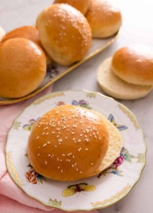 A plate with a brioche bun, sliced in half with more in the background on a platter.