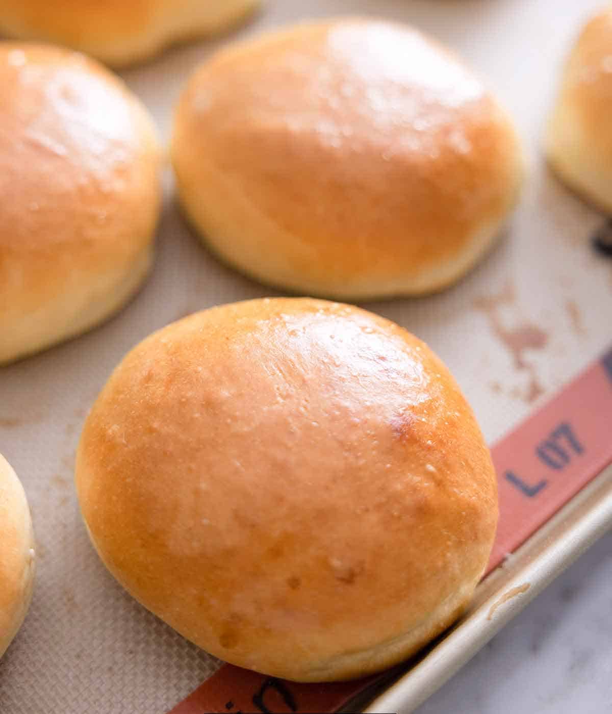 Close up of one brioche buns with more in the background on a sheet pan.