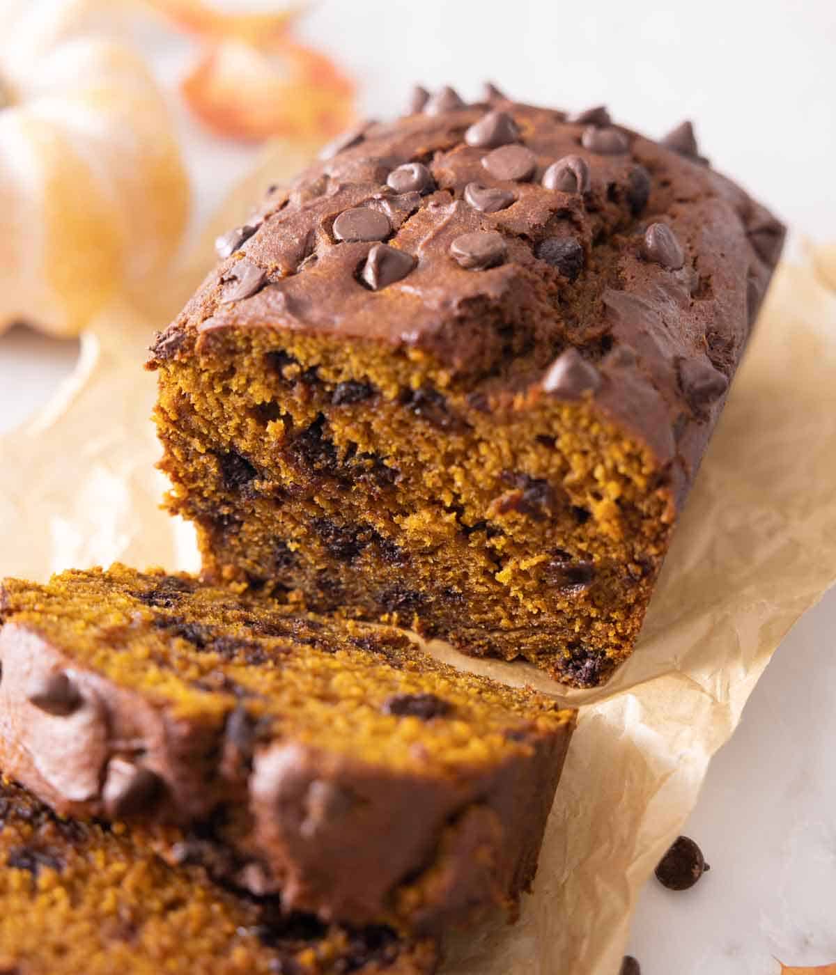 A loaf of chocolate chip pumpkin bread with two slices cut, showing the interior.