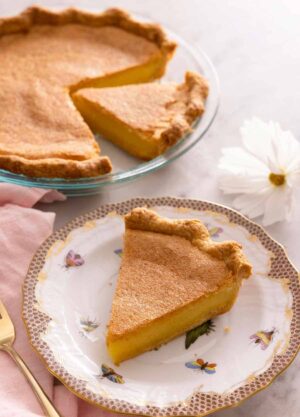 A slice of chess pie on a plate in front of the rest of the pie in the background.