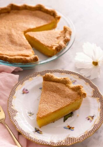 A slice of chess pie on a plate in front of the rest of the pie in the background.