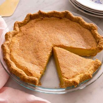 A chess pie in a glass pie dish with one slice cut out.