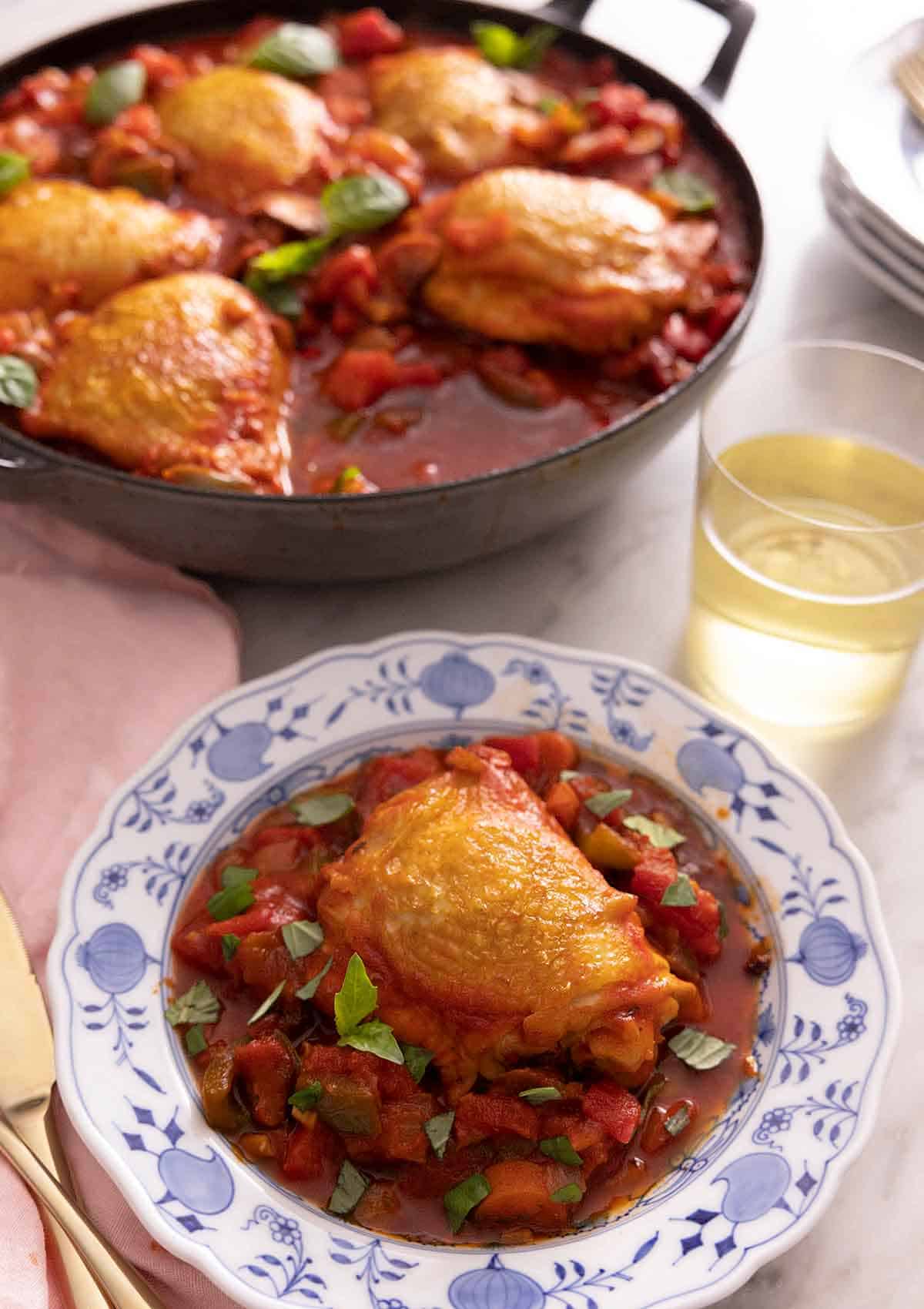 A plate with a serving of chicken cacciatore in front of a pan with more chicken.