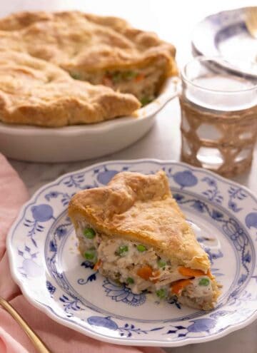 A plate of with a slice of chicken pot pie in front of a glass of water and the pie dish.
