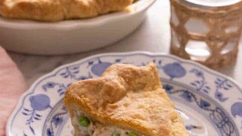 A plate of with a slice of chicken pot pie in front of a glass of water and the pie dish.