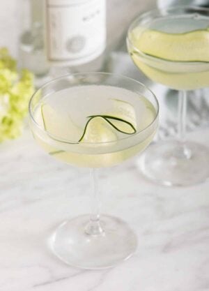 Two glasses of cucumber martini with one in front of the other. Both has a thin slice of cucumber as garnish.