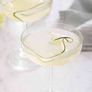 A glass of cucumber martini with a linen napkin in the background and a second martini out of focus.