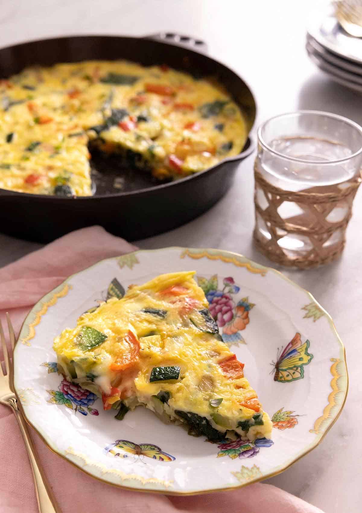 A plate with a slice of frittata with the skillet with the rest of the frittata in the background.