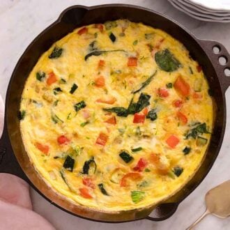 Overhead view of a frittata in a cast iron pan with a pink linen napkin beside with and a serving utensil.