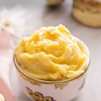 Pinterest graphic of a bowl of honey butter with biscuits in the background.