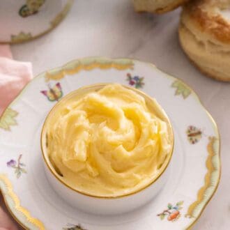 Pinterest graphic of a bowl of honey butter on a plate with two biscuits in the background.