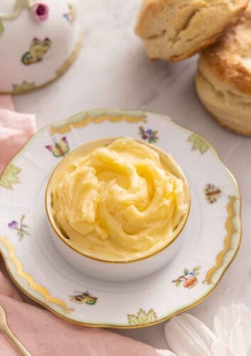 A bowl of honey butter on a plate with some biscuits in the background.