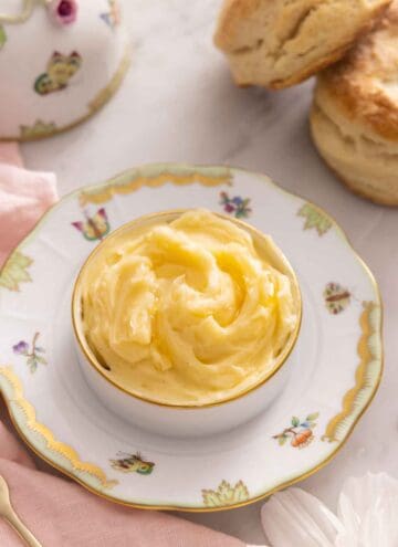 A bowl of honey butter on a plate with some biscuits in the background.