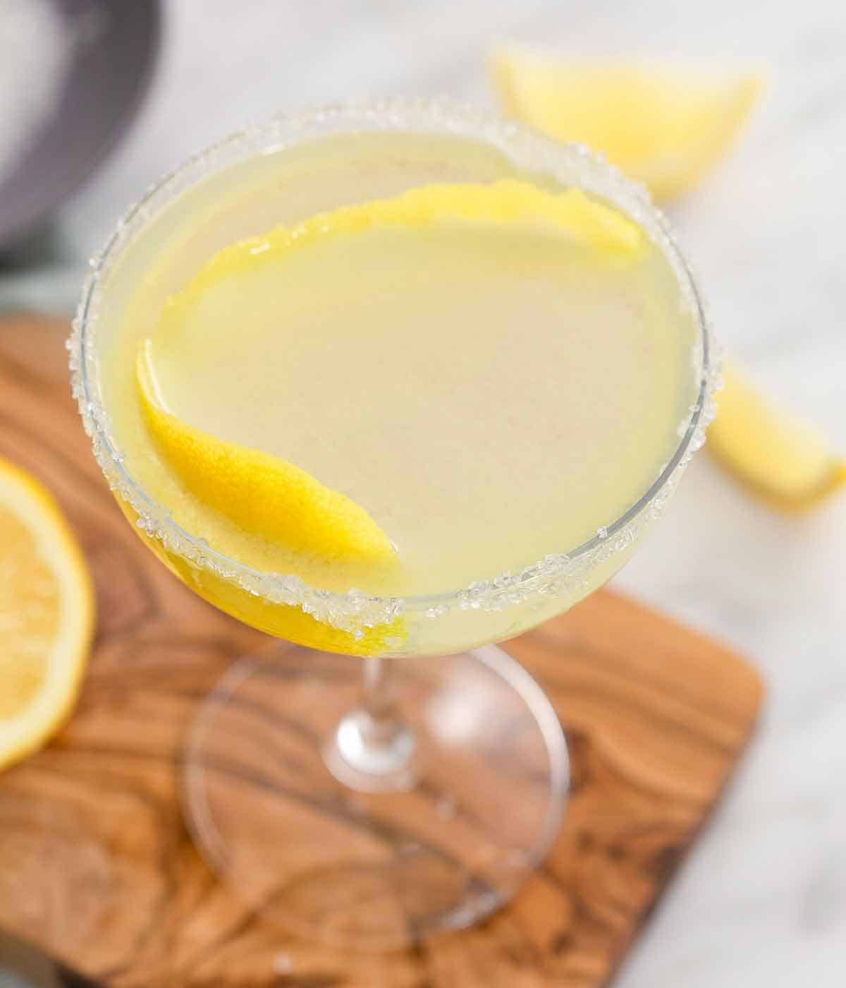 Angled view of a cocktail glass of a lemon drop martini with sugar on its rim and lemon peel in the drink.