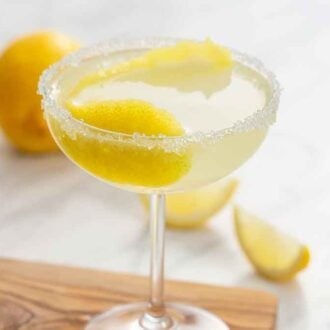 A glass of lemon drop martini on a cutting board with lemon wedges in the background.