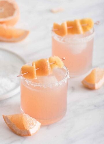 Two glasses of paloma with grapefruit peel as garnish on top.
