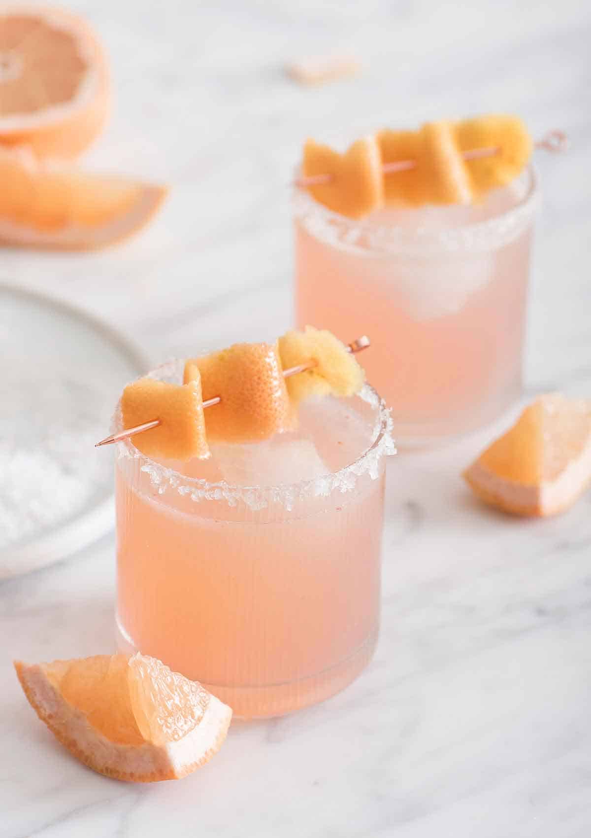 Two glasses of paloma with grapefruit peel as garnish on top.