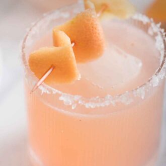 Pinterest graphic of an angled overhead view of a glass of paloma with salt on the rims and a peel as garnish.