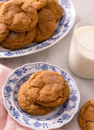 A plate with two pumpkin snickerdoodles with a larger plate containing more behind it with a glass of milk.