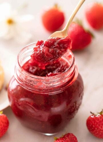 A mason jar filled with strawberry jam with a spoonful scooped out.