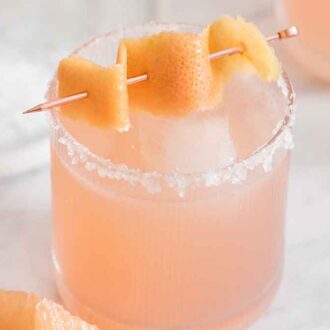 A glass of paloma with salt on the rim and a grapefruit peel as garnish.