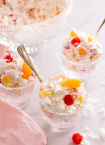 Three cups of ambrosia salad with spoons inserted beside a pink linen napkin.