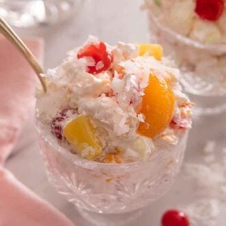 Close up of one cup of ambrosia salad with shredded coconut flakes on top.