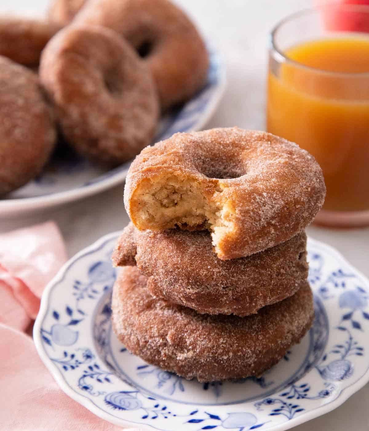 A stack of three apple cider donuts with the top one with a bite taken out of it.
