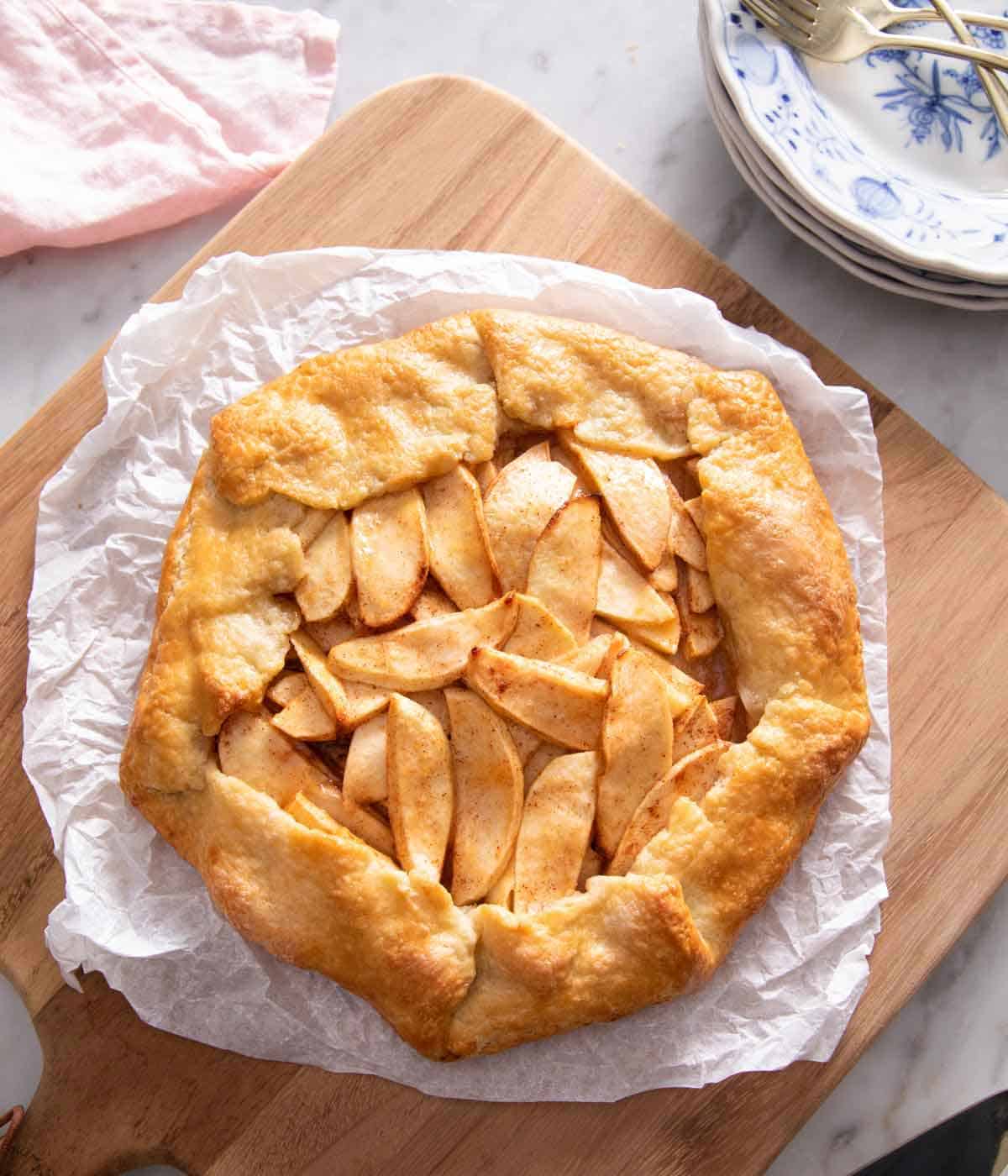 Overhead view of an apple galette on a sheet of parchment paper on a wooden serving board.