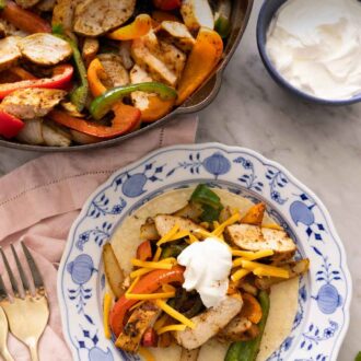 Pinterest graphic of a plate of chicken fajitas on a tortilla in front of a skillet with the rest of the chicken fajitas.