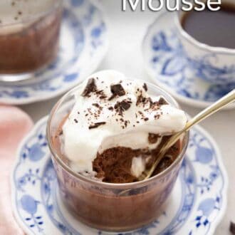 Pinterest graphic of a glass of chocolate mousse with whipped cream and shaved chocolate with a spoonful eaten and a spoon inside.