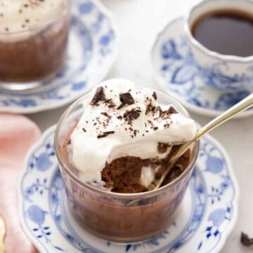 A glass of chocolate mousse with whipped cream and shaved chocolate with a spoonful eaten and a spoon inside.