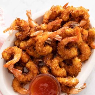 An oval platter with coconut shrimps with a small bowl of sauce on the side.