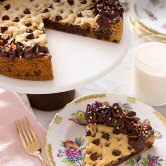 Pinterest graphic of a cookie cake on a cake stand with a slice cut and served on a plate in front.
