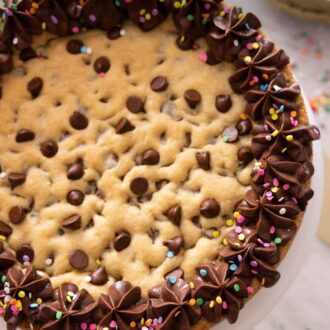 Pinterest graphic of an overhead view of a cookie cake with chocolate frosting piped topped with sprinkles.