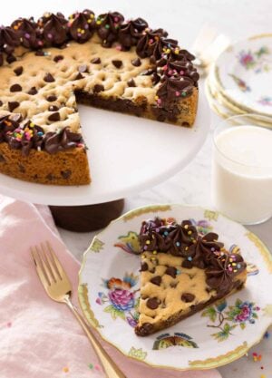 A cake stand with a cookie cake with a slice removed and placed on a plate.