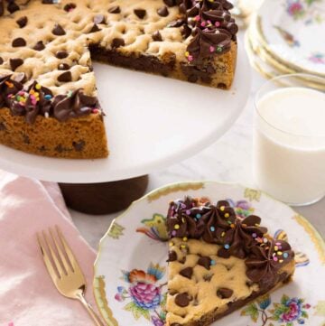 A cake stand with a cookie cake with a slice removed and placed on a plate.