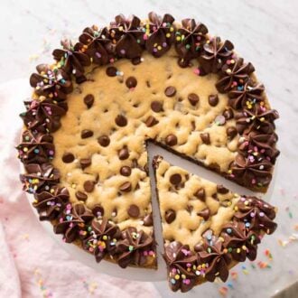 Overhead view of a cookie cake with a slice cut and slid out with sprinkles scattered around.